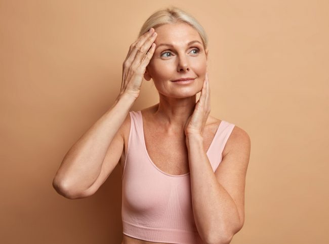Portrait of mature elderly European woman touches face gently has perfect skin and looks thoughtfully away enjoys her soft complexion cares about appearance satisfied after anti aging procedure consejos para cuidar la piel a partir de los 40